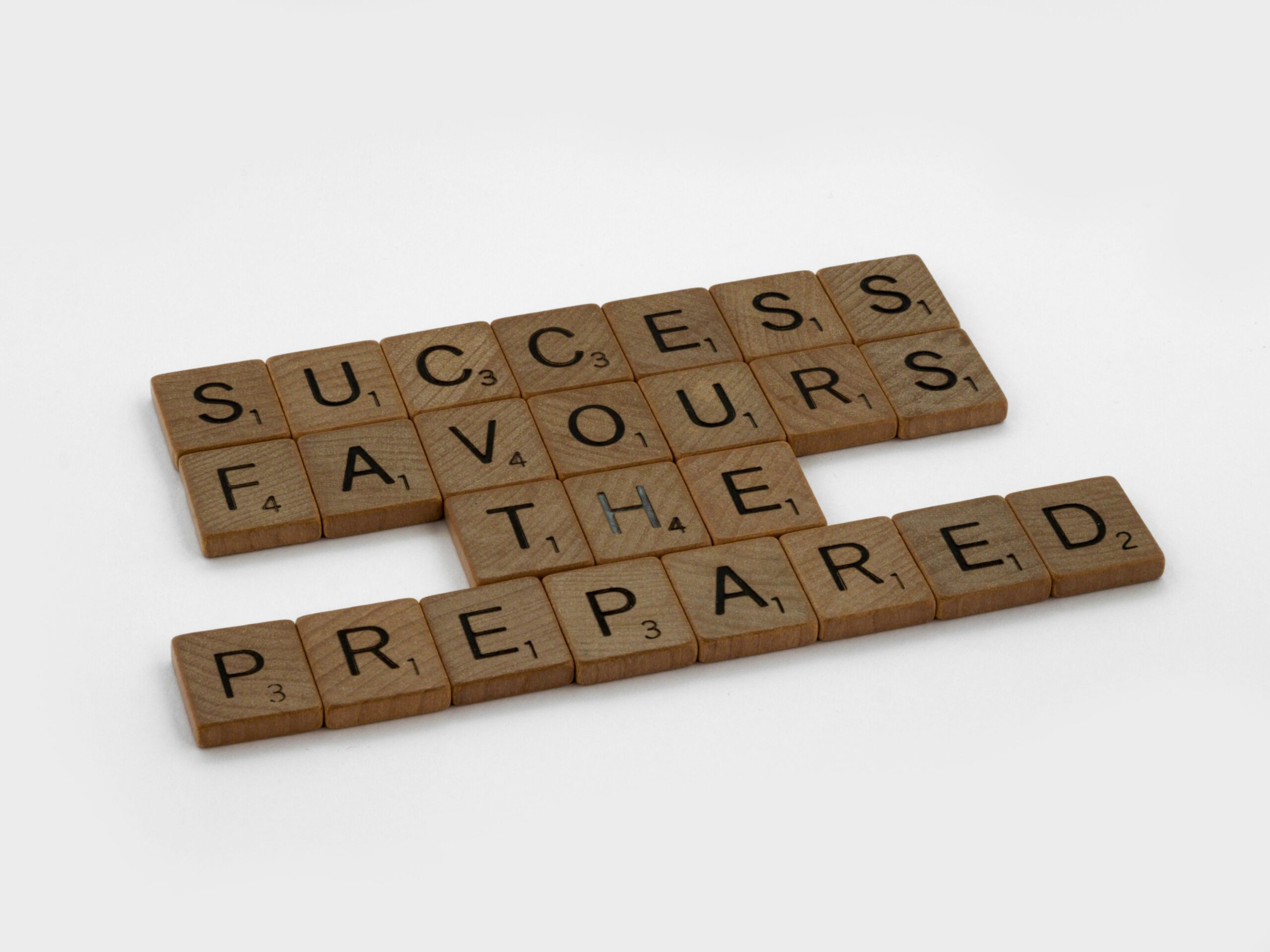 Scrabble tiles on a white surface forming the phrase 'Success Favours the Prepared'.