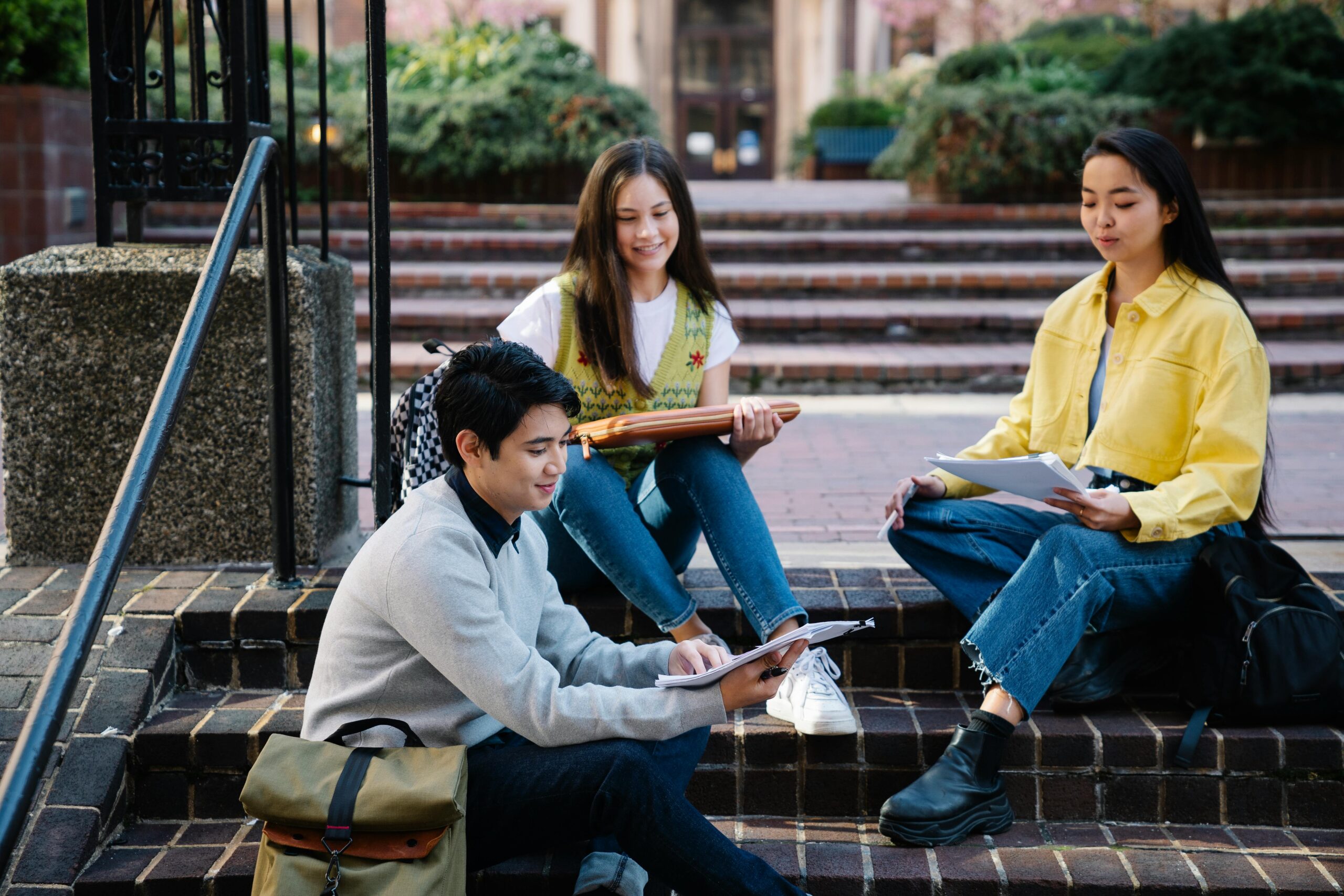 Group of students studying outdoors on college campus steps, enjoying sunny day.