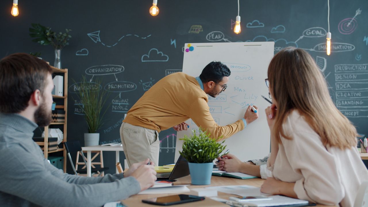 Diverse team collaborating in a creative office, brainstorming ideas on a whiteboard.